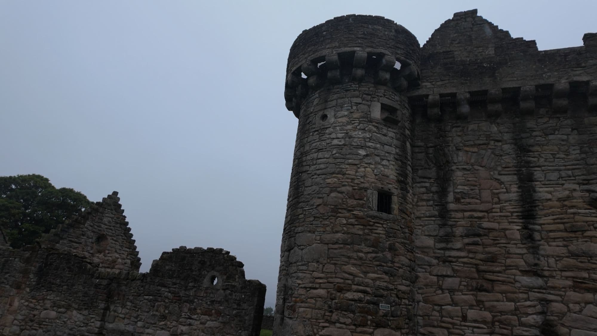 A round corner tower on Craigmillar's curtain wall, dark against an overcast sky