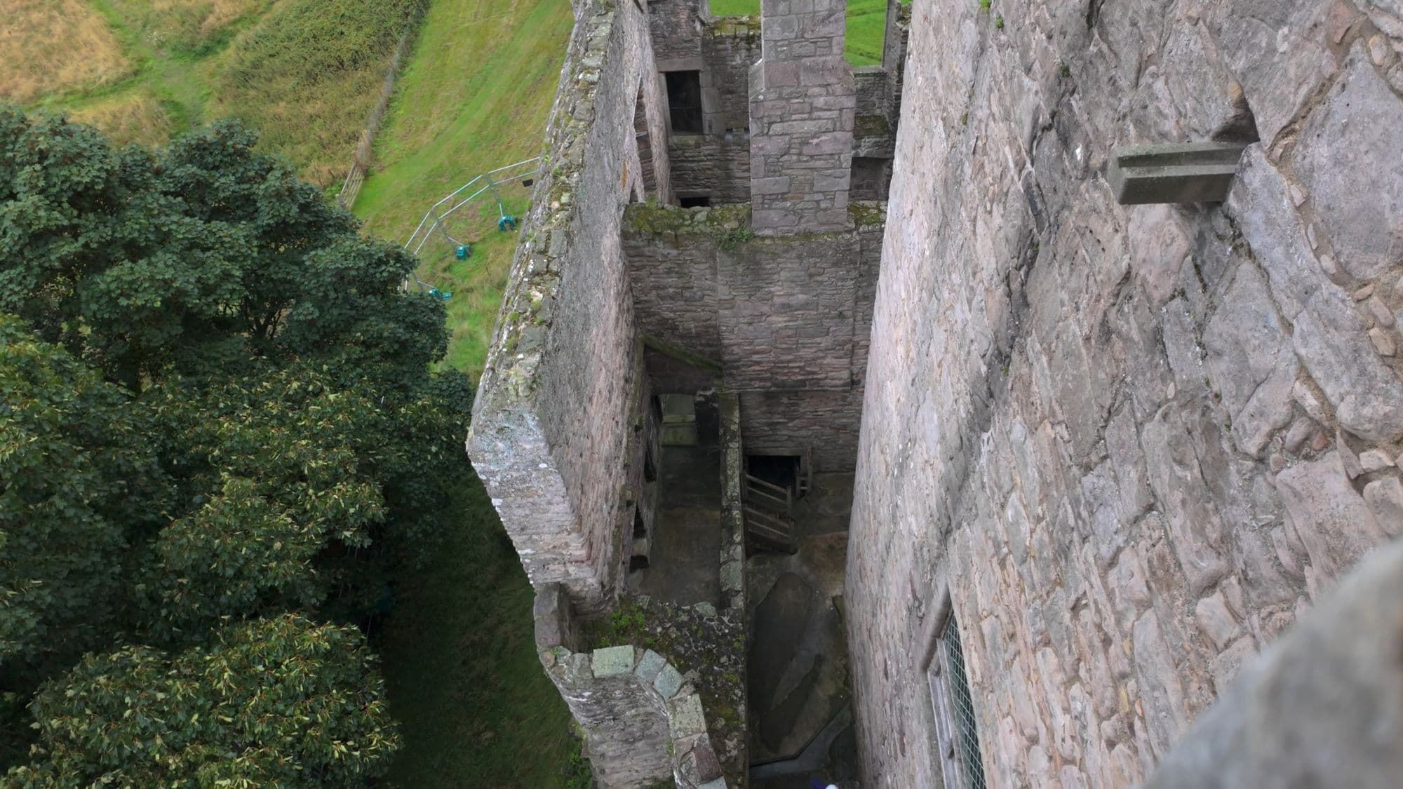 Looking straight down from the tower into the roofless ranges below, the castle walls dropping away toward the grass