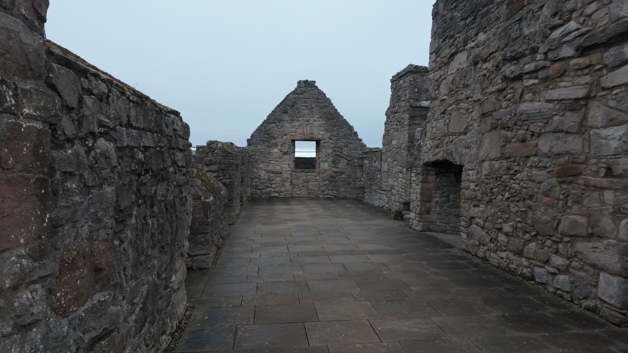 The paved rooftop walkway of the tower house, enclosed by stone parapets and a gabled end wall