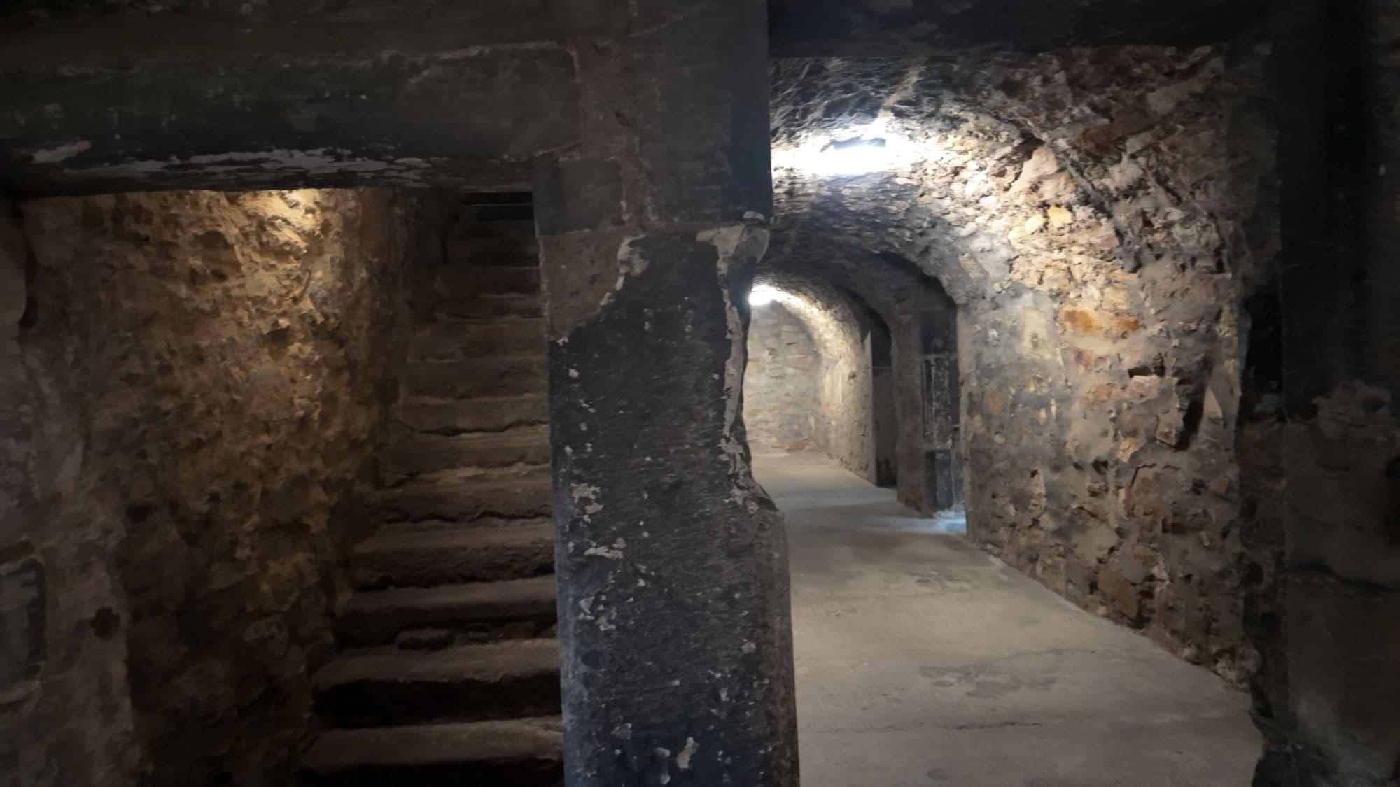 A stone stair and a lit, vaulted passage running through the lower levels of the castle