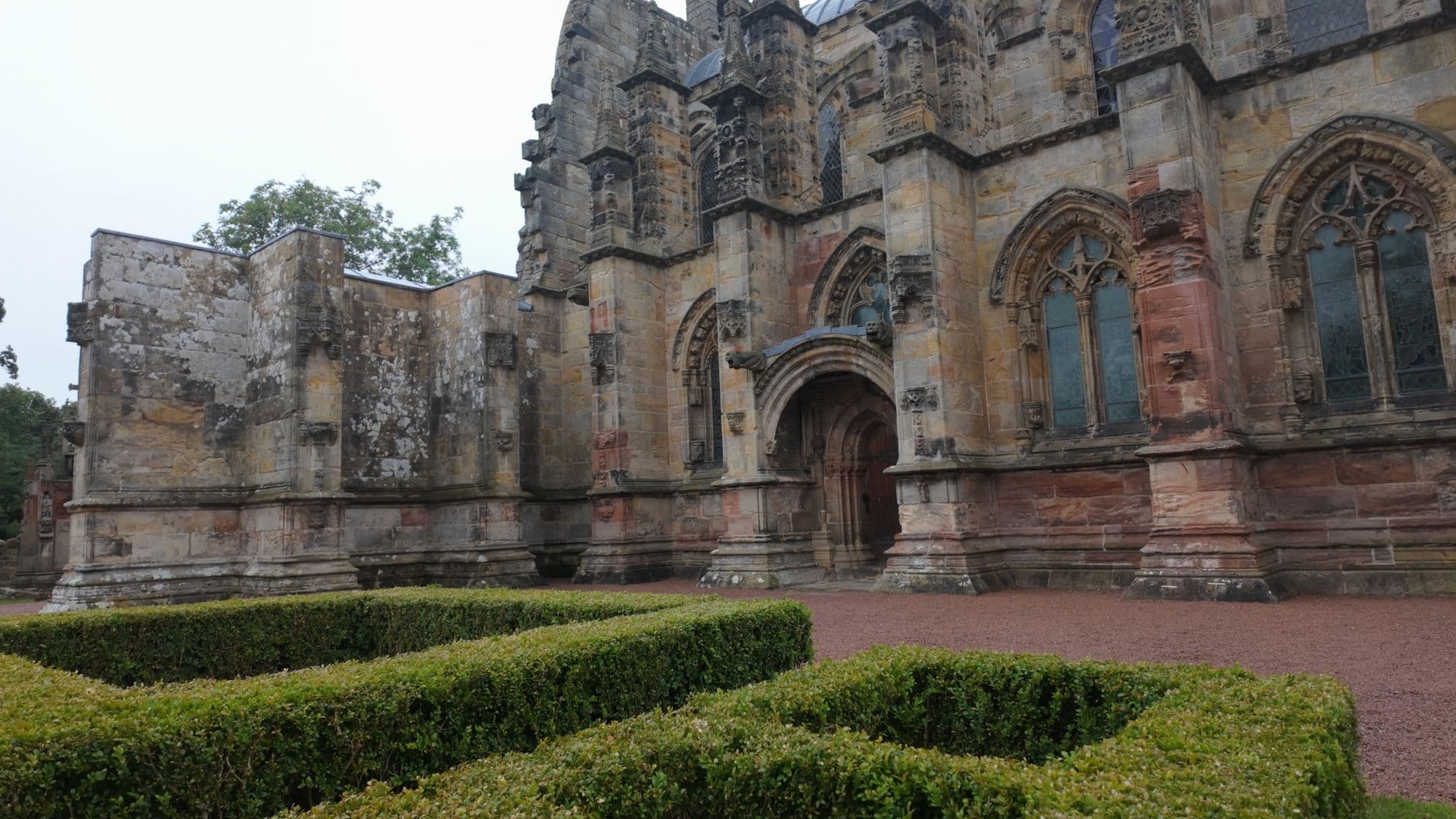 The chapel's red-and-gray sandstone side wall behind clipped box hedges