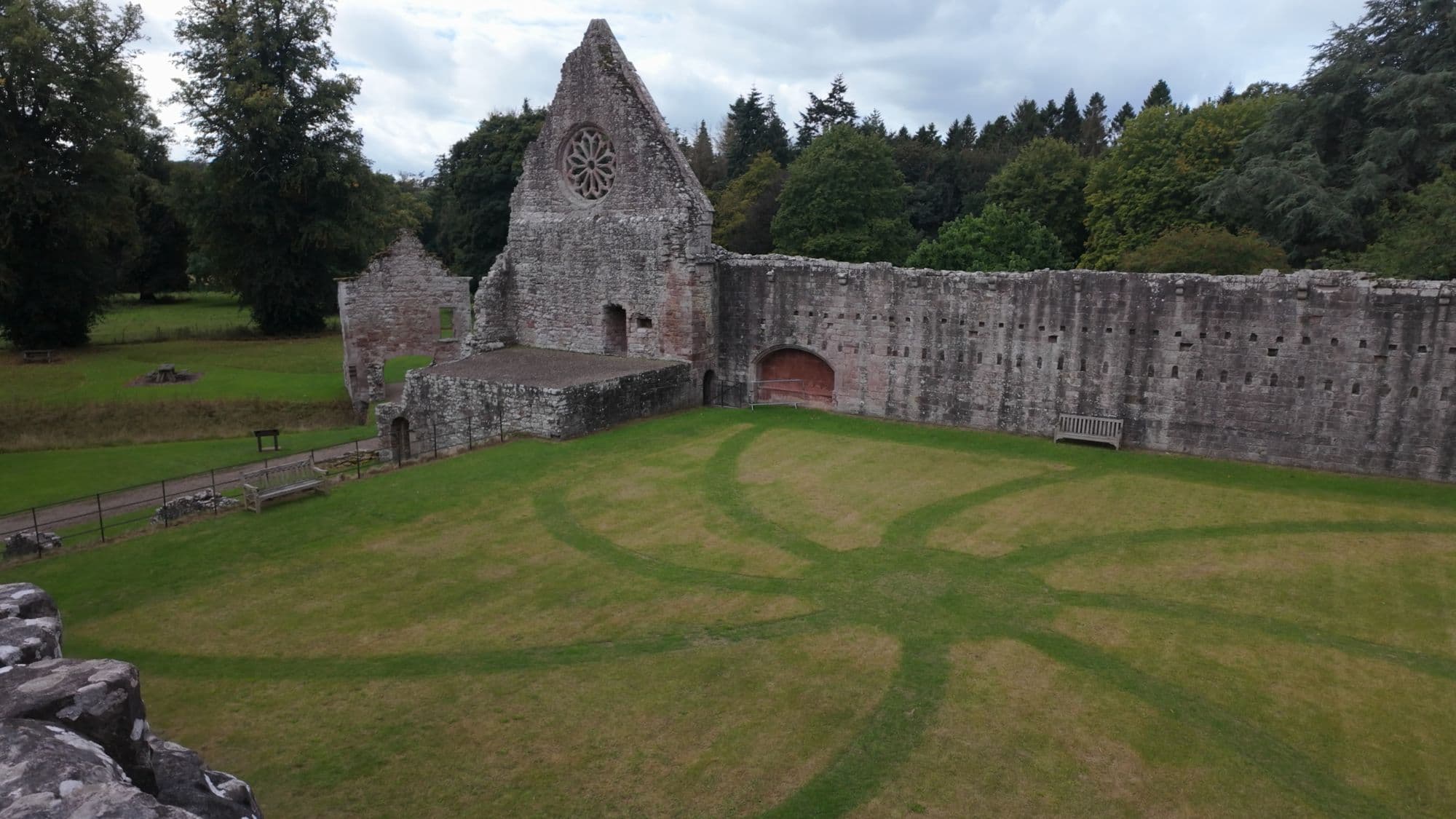 The refectory gable and the long cloister wall at Dryburgh across a mown lawn