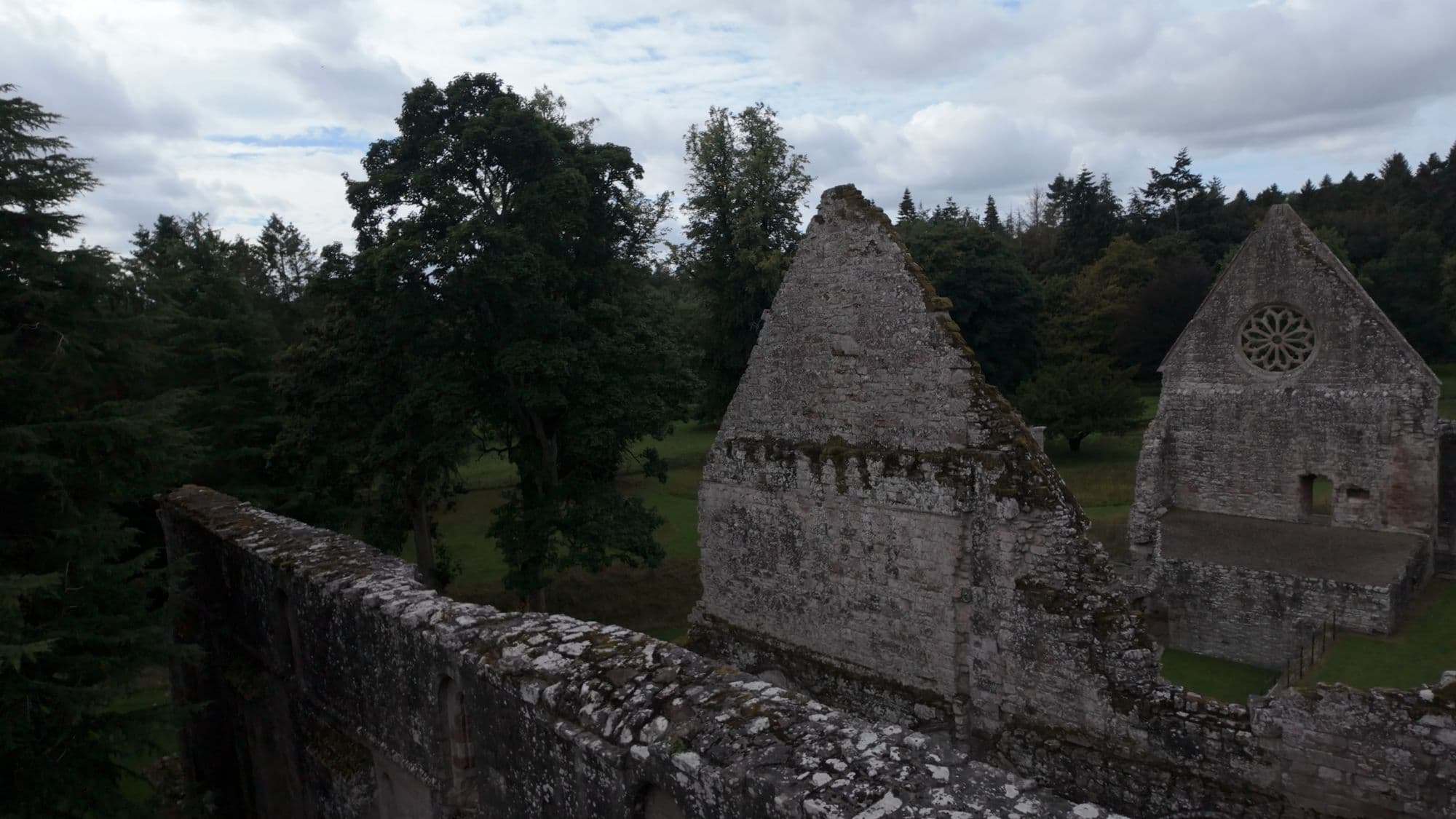 Two ruined gables at Dryburgh seen over a crumbling wall, with woodland behind