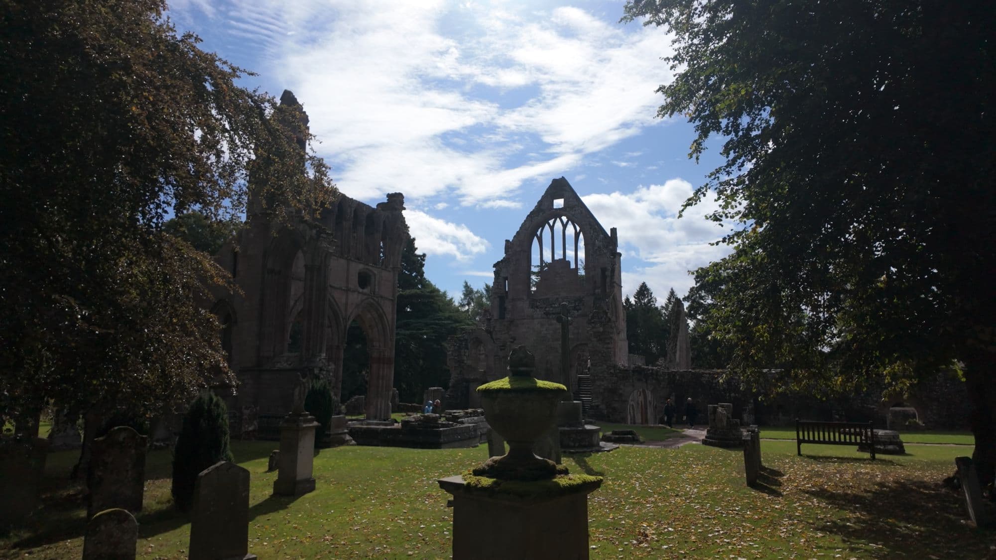 Gravestones and an urn-topped monument in the Dryburgh churchyard, the abbey gable behind
