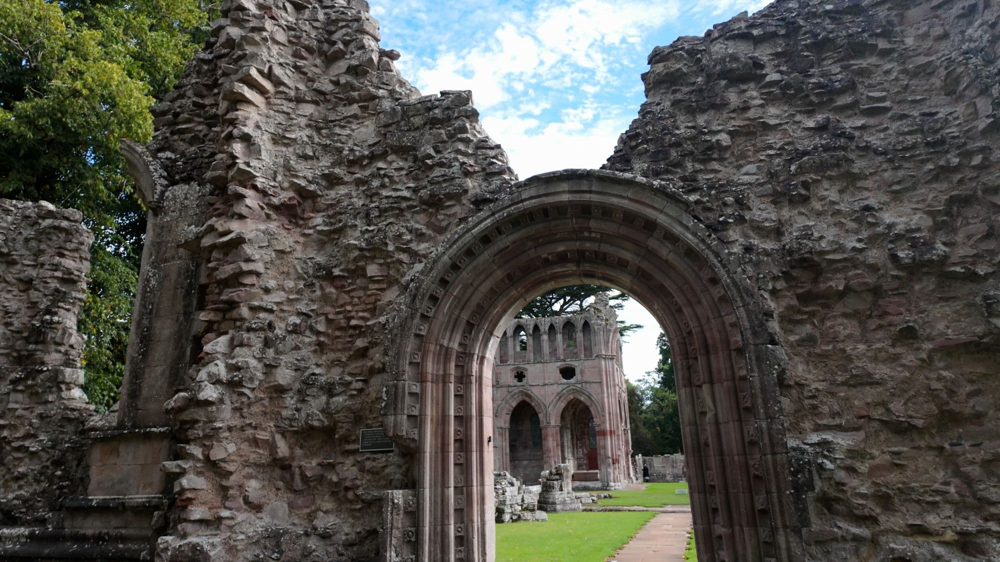 A round-headed doorway in a ruined wall, framing a view of the church arcade beyond