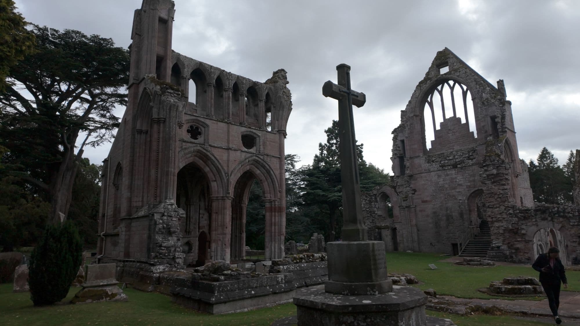 The pink sandstone transept of Dryburgh with a stone cross on a plinth in front of it