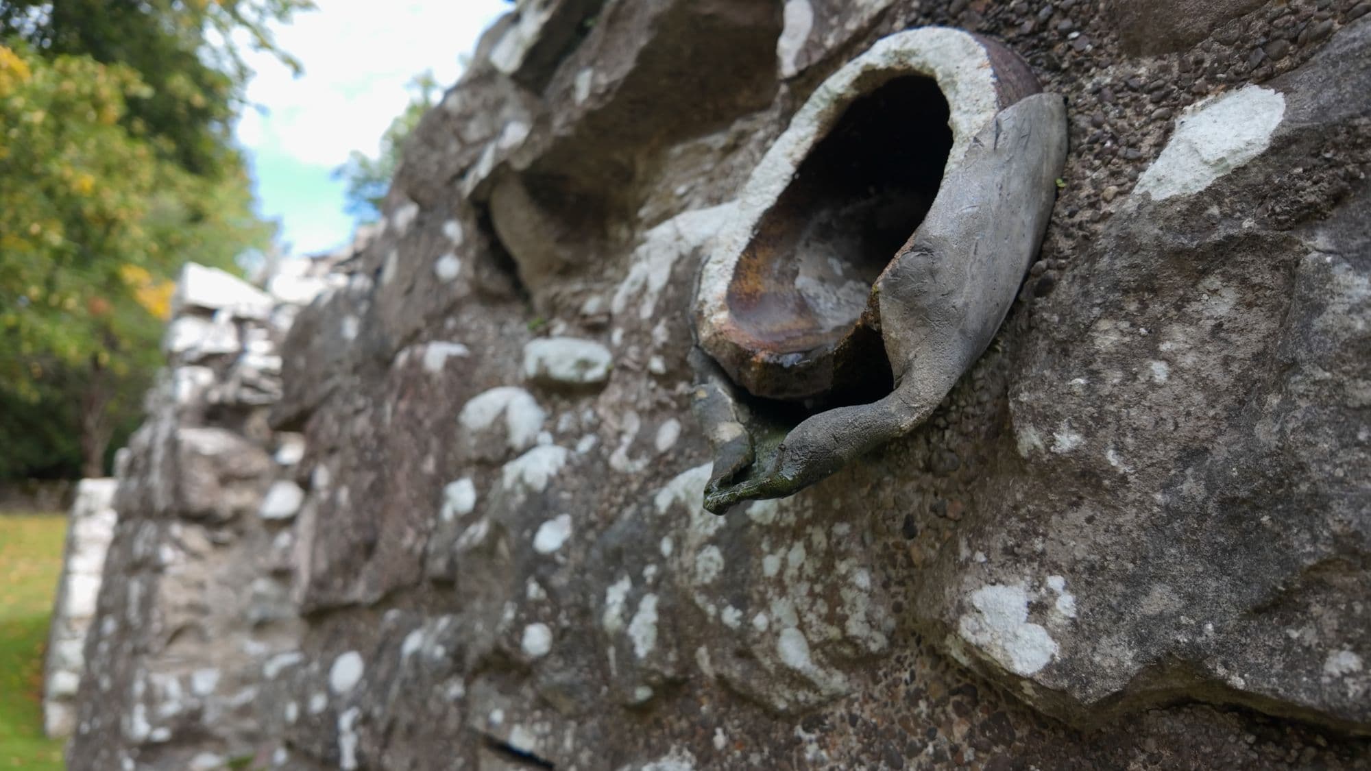 A carved stone water spout projecting from a lichen-covered wall