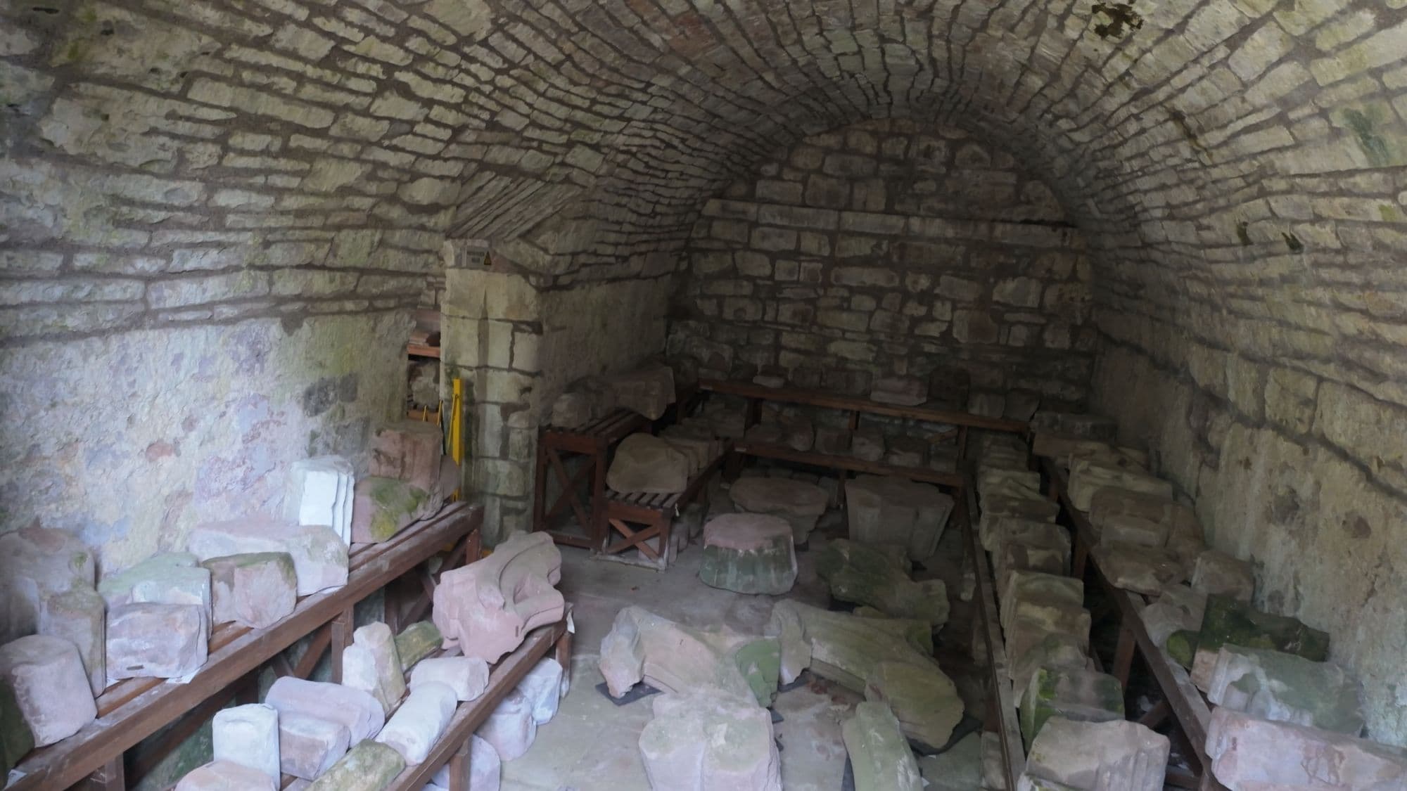 A barrel-vaulted room in the east range stacked with numbered fragments of carved stone from the abbey