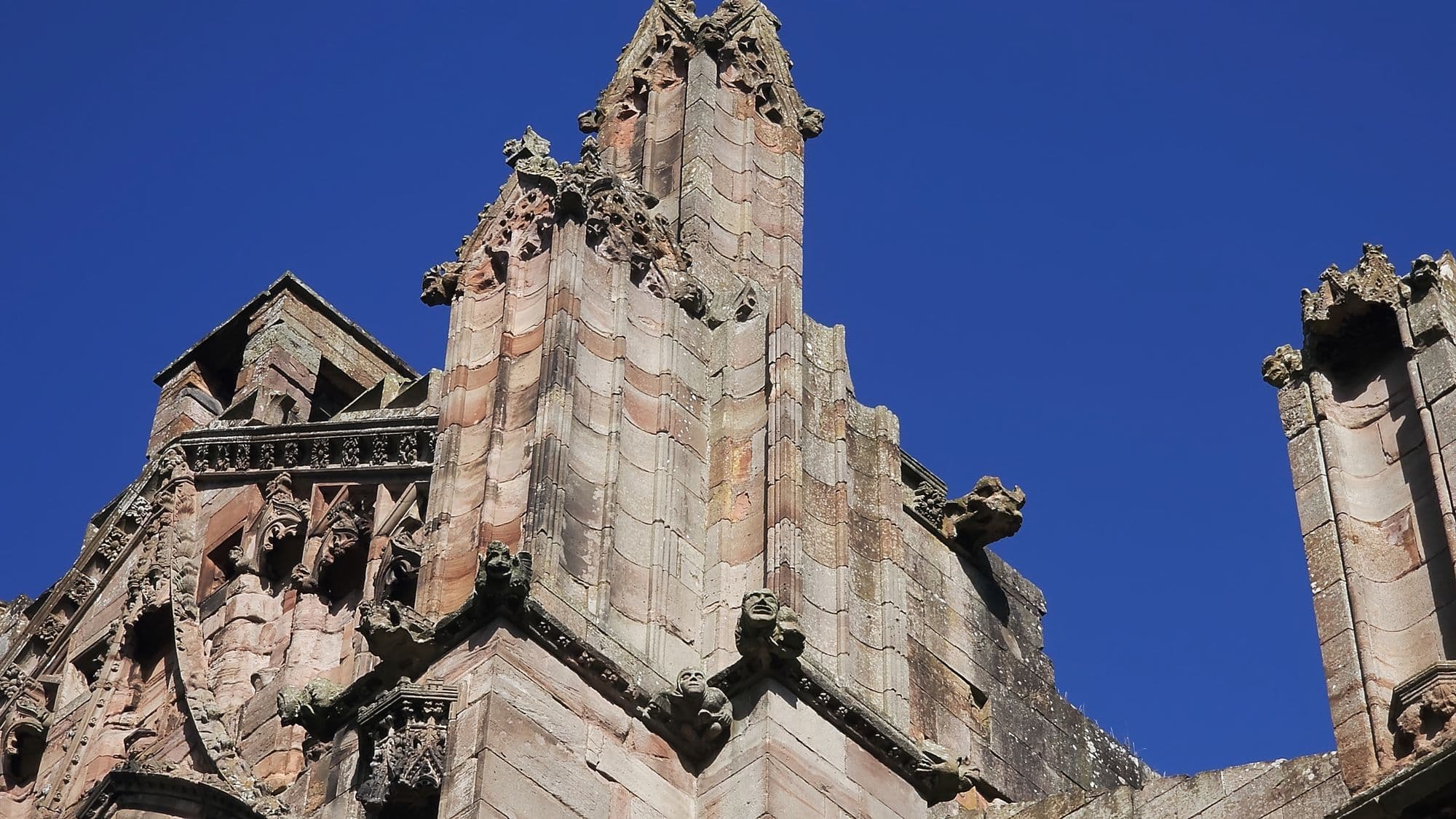 Pinnacles and gargoyles crowding the top of a buttress at Melrose, sharp against a deep blue sky