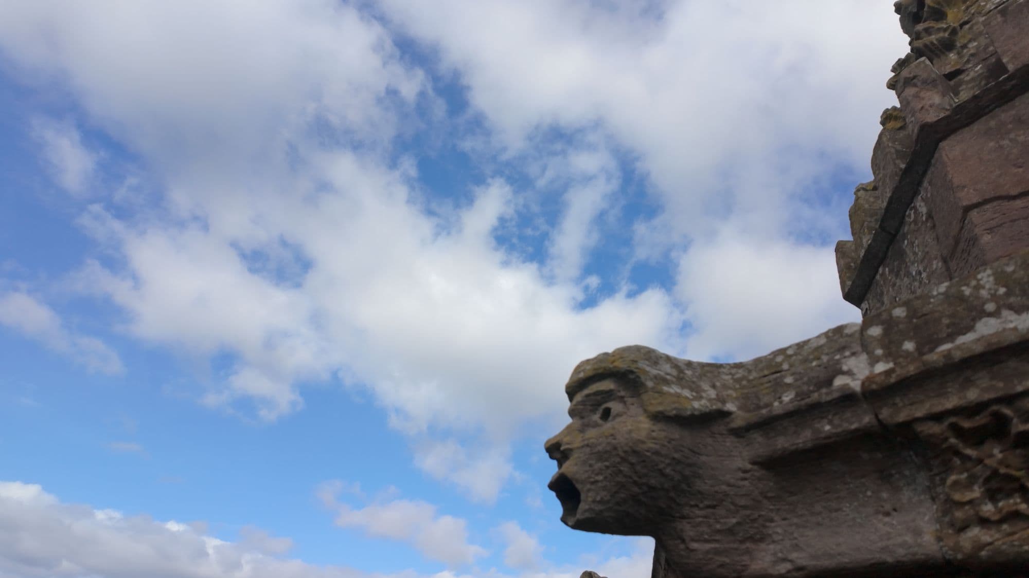 A carved face with a gaping mouth jutting out from the abbey wall as a gutter spout