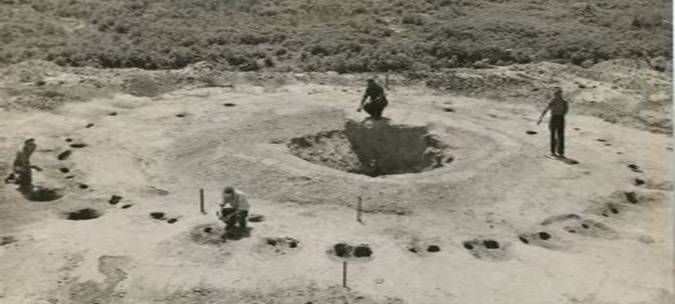 The excavation in progress: four workers around a stripped circular floor, a ring of dark postmolds marking where the walls of the building once stood