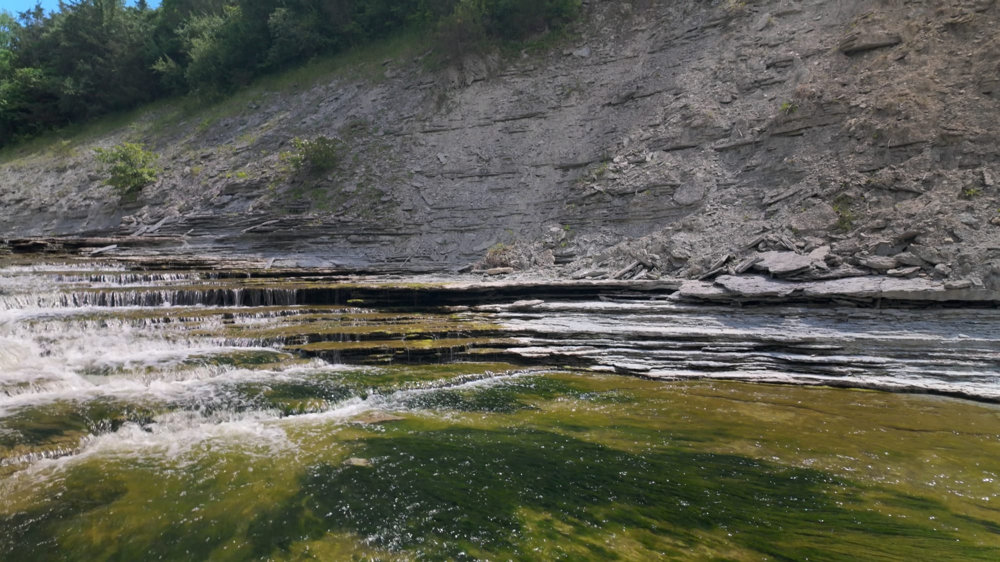 The spillway gorge below Cowan Lake — a tall wall of layered gray limestone above stepped shelves of rock the creek pours over