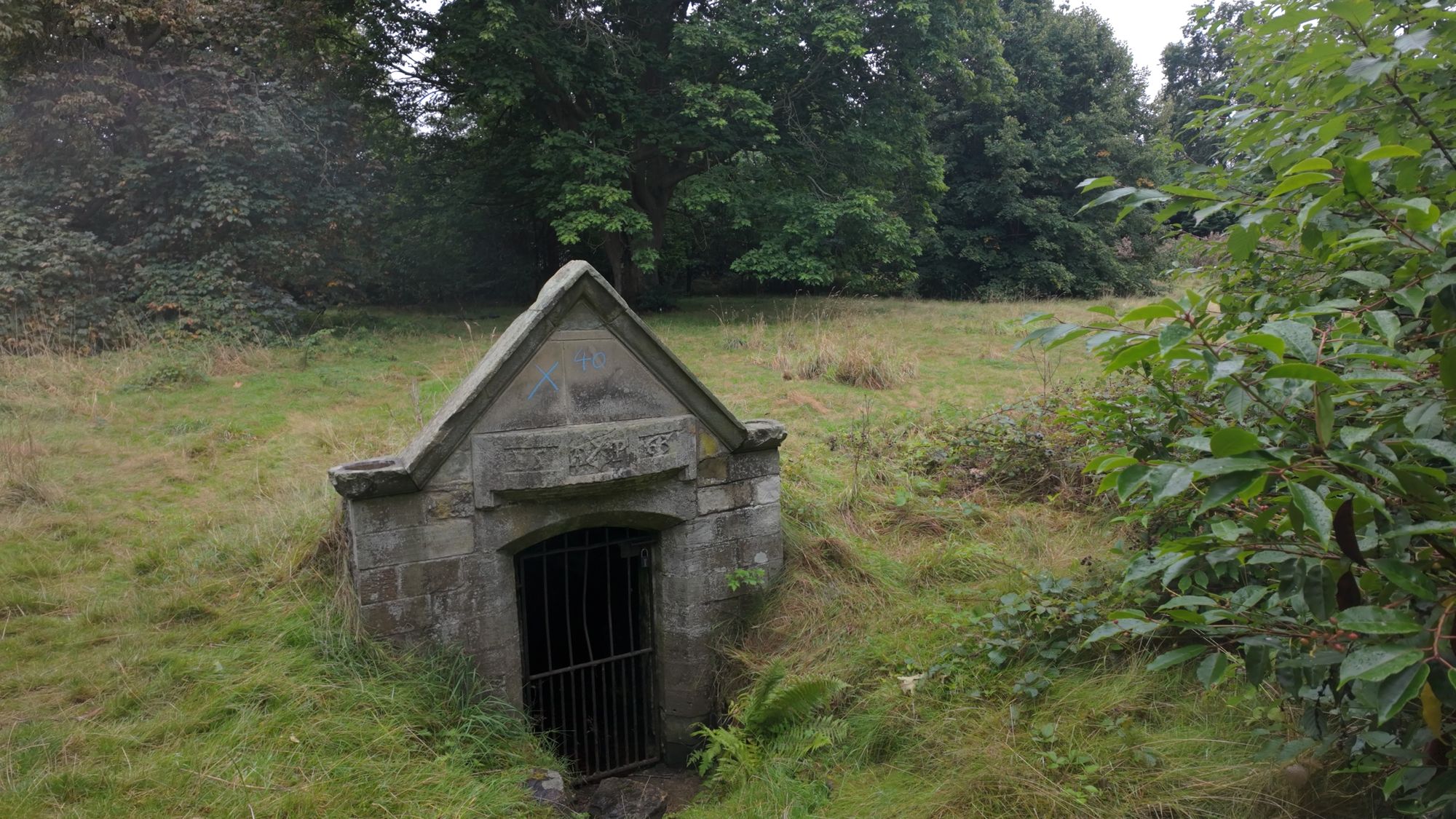 St Catherine's Balm Well in Liberton — a small gabled stone well house with an iron-barred door, half sunk into an overgrown meadow