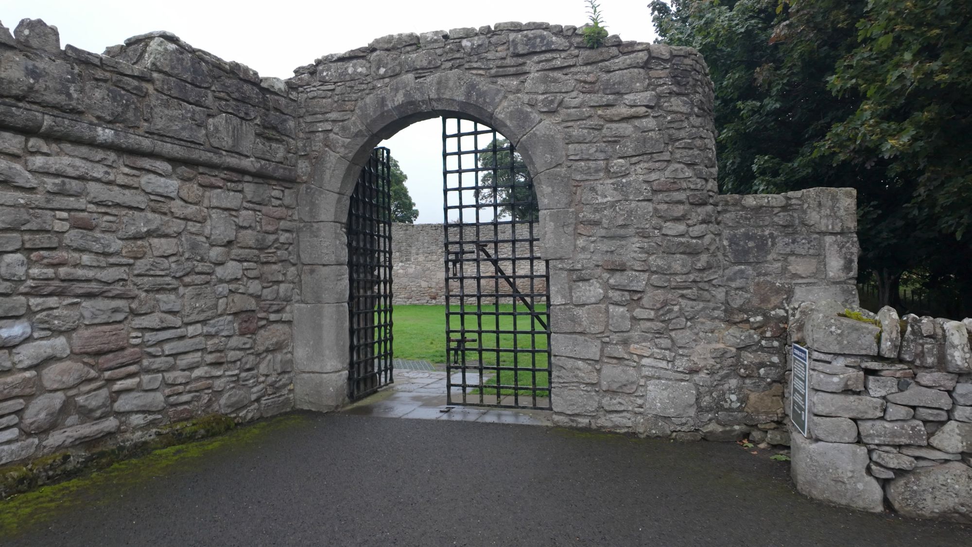 The arched outer gateway of Craigmillar Castle with its iron yett standing open onto the grass