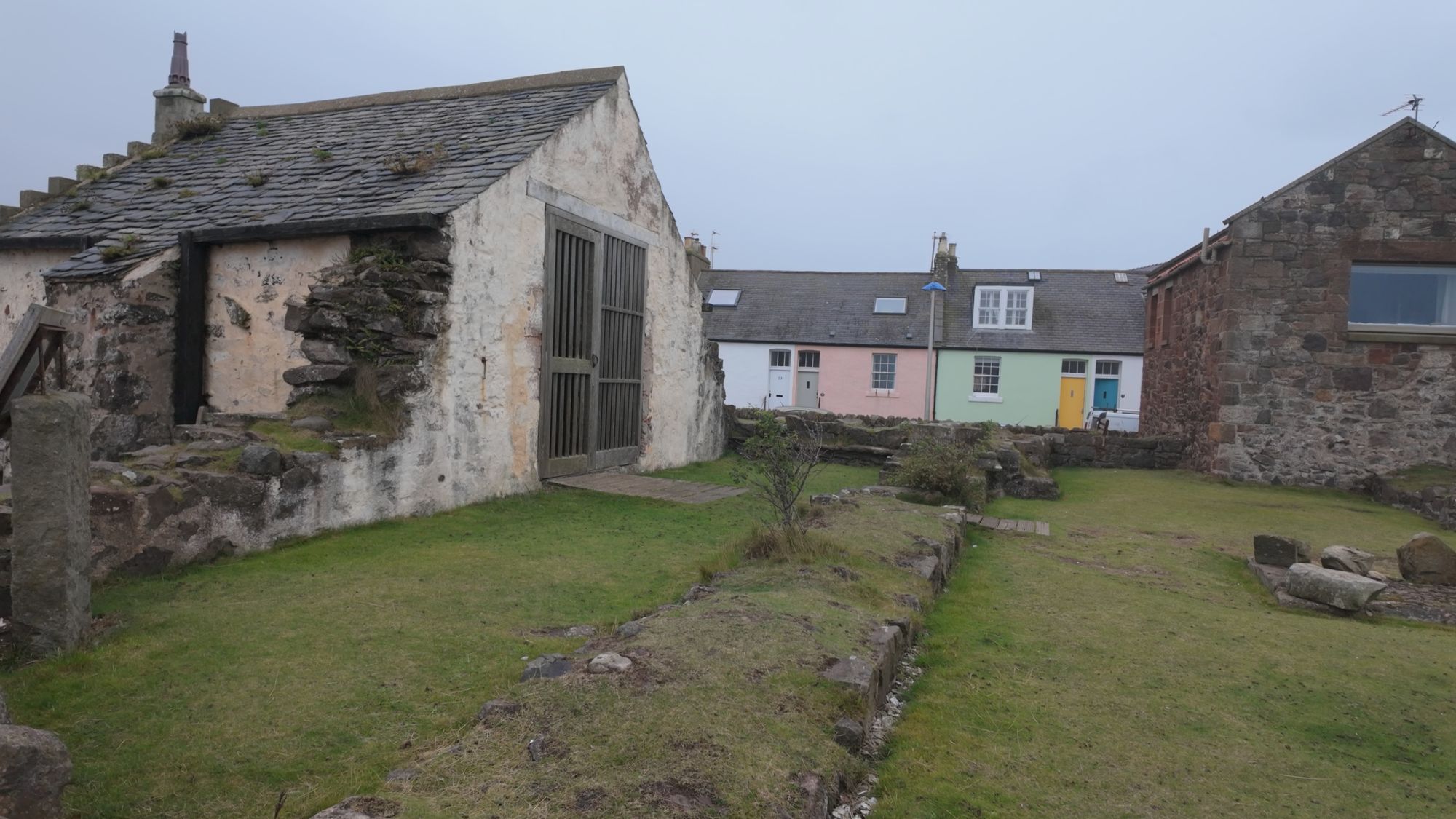 St Andrew's Old Kirk in Gullane — a low, whitewashed ruin with a barred gate, a row of colorful cottages behind it