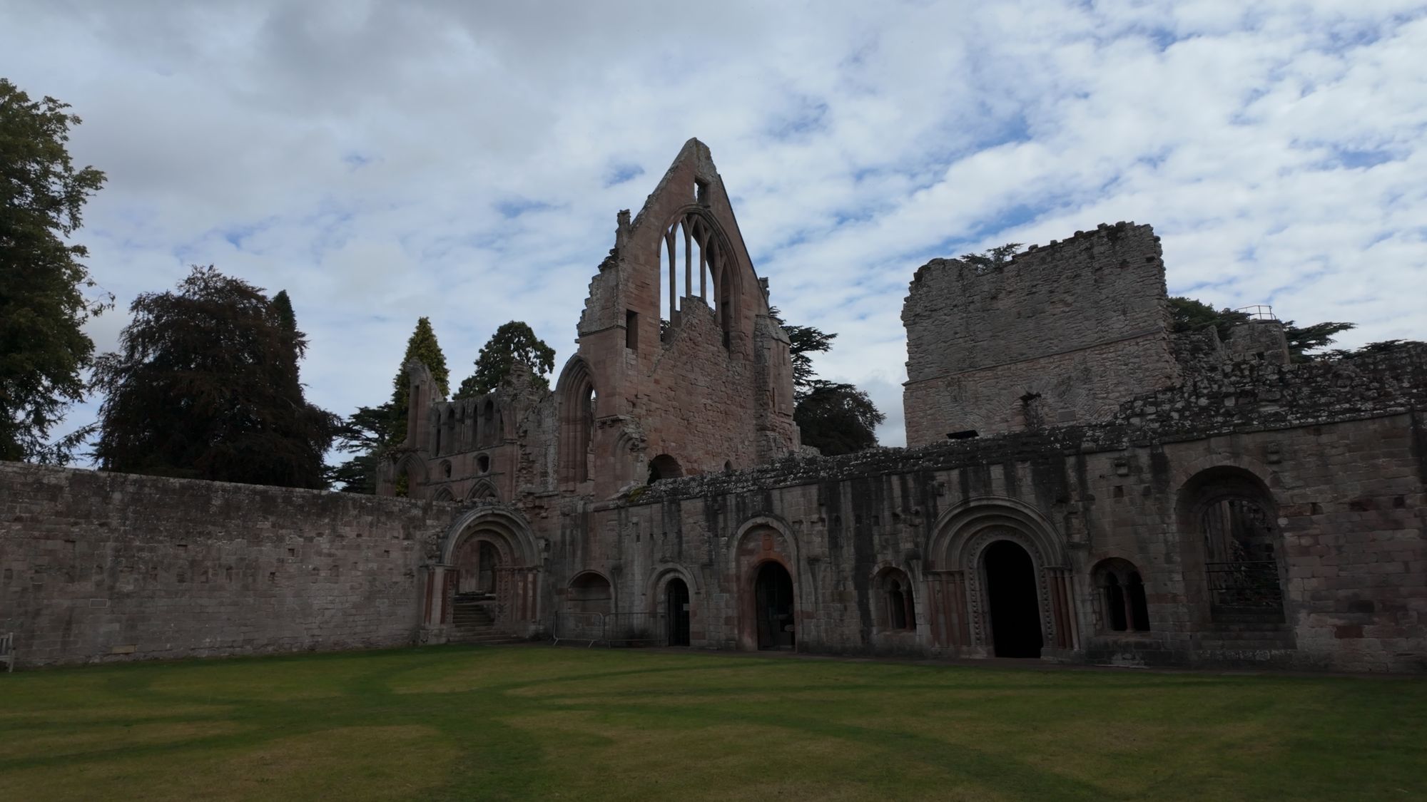 The east range of the cloister at Dryburgh, a long two-storey wall of doorways and windows facing an open lawn