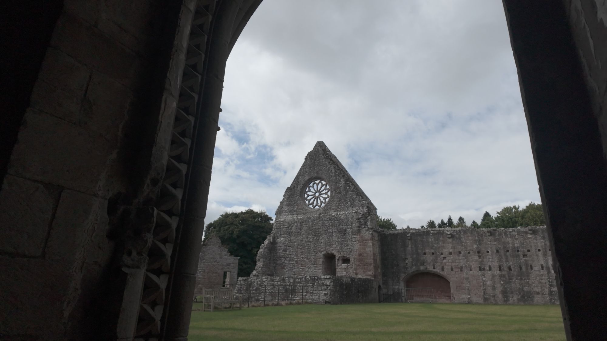 The rose window gable seen across the lawn from inside a dark doorway