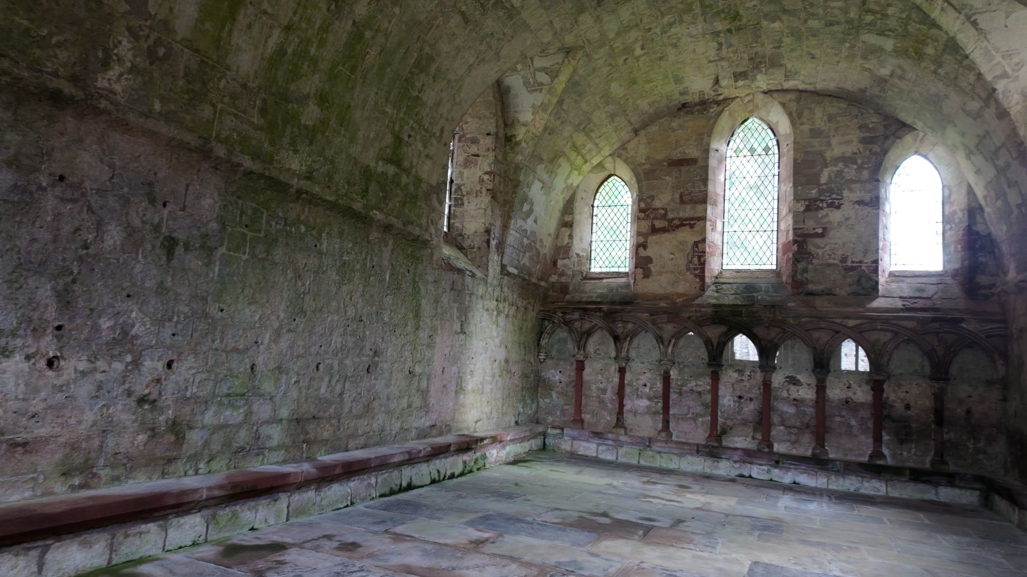 Inside the vaulted chapter house: a stone bench along the walls and an arcade of small arches still carrying traces of old red paint