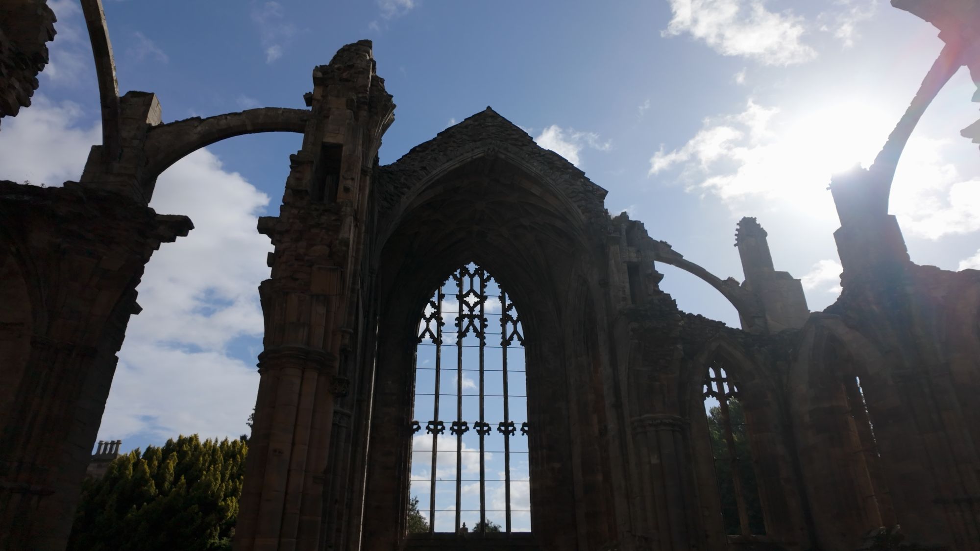 The great east window of Melrose silhouetted against a bright sky, its tracery black against the clouds