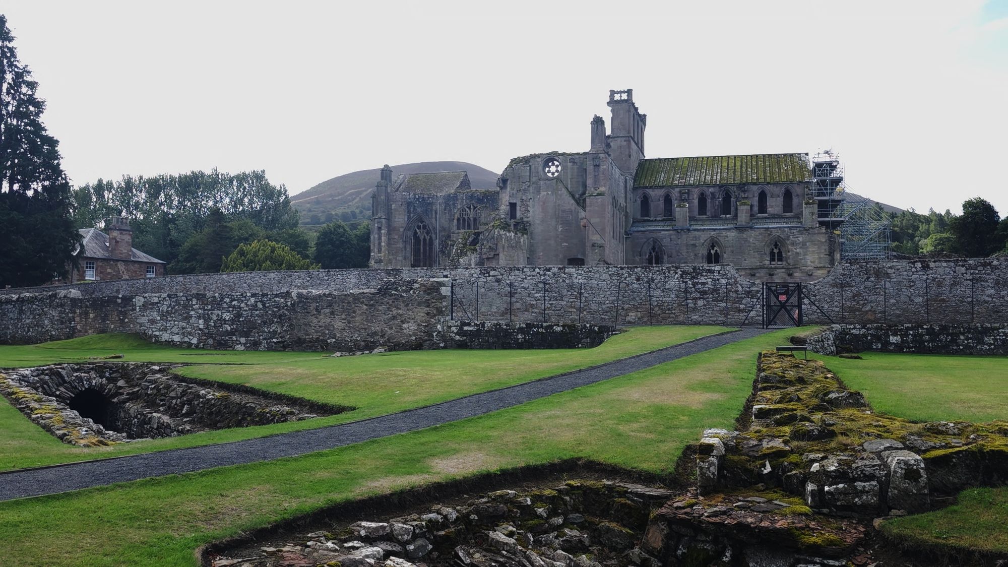 Melrose Abbey across its excavated cloister foundations, with one of the Eildon Hills rising behind it
