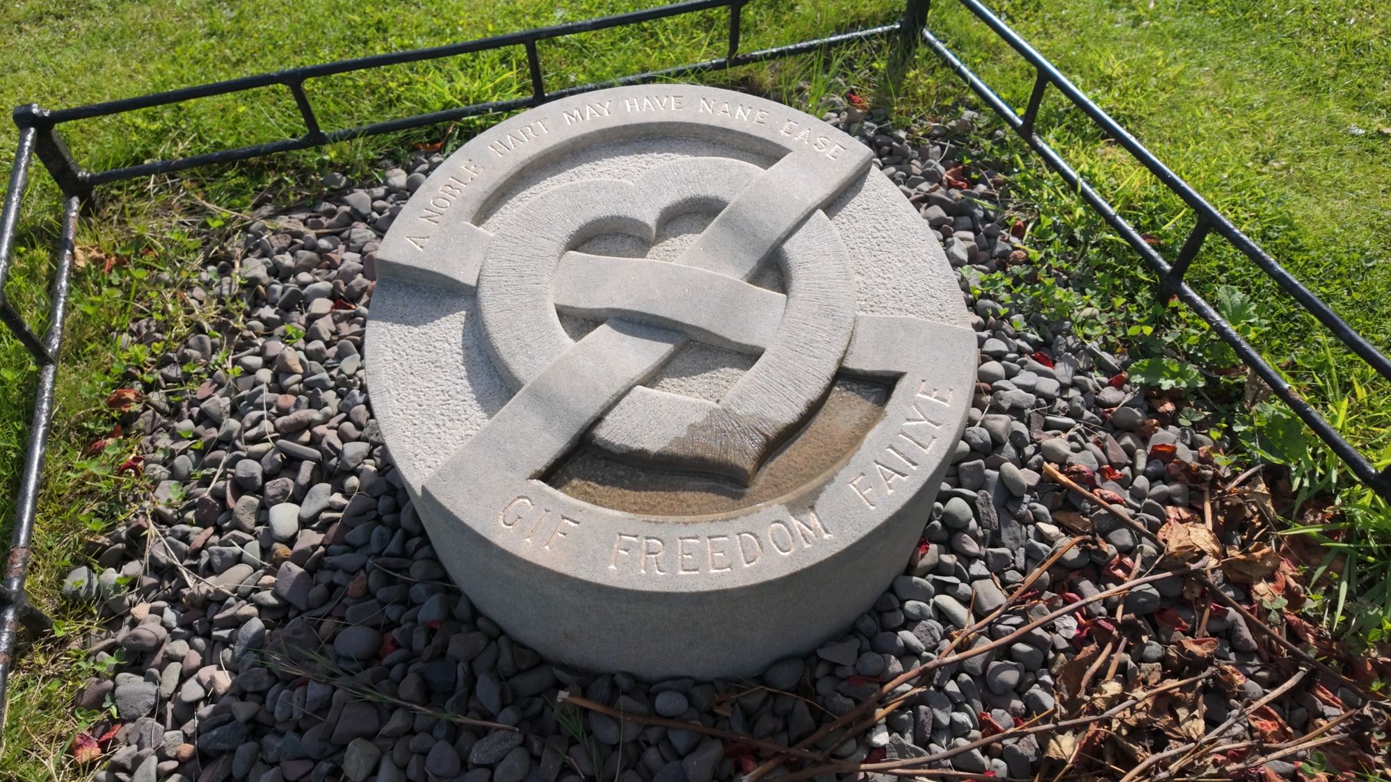 The round memorial stone over Bruce's heart, carved with an interlaced heart and the words of John Barbour's poem, inside a low railing